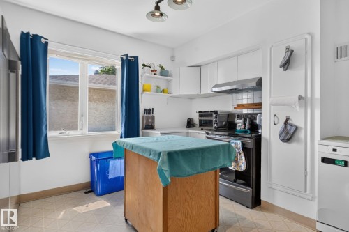Bright kitchen featuring white cabinetry, a large window, a stainless steel range hood, a tiled backsplash, and light-toned patterned flooring - 12229 88 Street Nw, Edmonton, AB - Indoor Photo Showing Kitchen