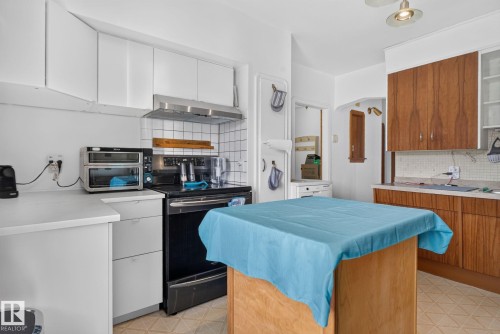 Kitchen featuring white upper cabinetry, a stainless steel range hood, a white tile backsplash, and wood-finish lower cabinetry - 12229 88 Street Nw, Edmonton, AB - Indoor