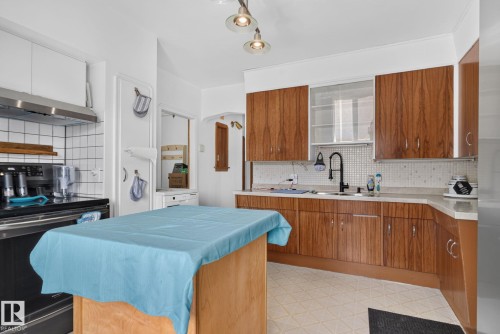 Kitchen featuring wood-finish cabinetry, white tile backsplash, and light-toned countertops - 12229 88 Street Nw, Edmonton, AB - Indoor Photo Showing Kitchen With Double Sink