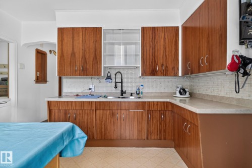 Kitchen featuring wood-grain cabinetry, light-toned countertops, and a mosaic tile backsplash - 12229 88 Street Nw, Edmonton, AB - Indoor Photo Showing Kitchen With Double Sink