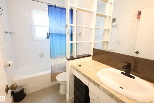 Bathroom featuring a white bathtub, ceramic wall tiling, built-in shelving, a vanity with a tile countertop, and a white basin with a matte black faucet - 12229 88 Street Nw, Edmonton, AB - Indoor Photo Showing Bathroom