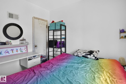 White walls featuring a built-in wall desk with a single drawer, a circular mirror, and an overhead air vent - 12229 88 Street Nw, Edmonton, AB - Indoor Photo Showing Bedroom