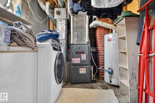 Laundry area featuring a front-load washing machine, a water heater, a furnace unit, exposed brick, and built-in shelving - 12229 88 Street Nw, Edmonton, AB - Indoor Photo Showing Laundry Room