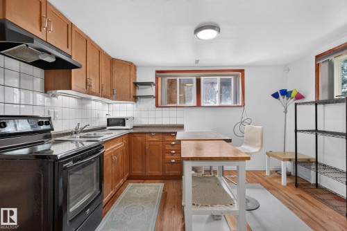 Kitchen featuring wood cabinetry, white tile backsplash, black appliances, a double basin sink, and wood-finish flooring - 12229 88 Street Nw, Edmonton, AB - Indoor Photo Showing Kitchen With Double Sink