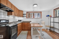 Kitchen featuring wood cabinetry, white tile backsplash, black appliances, a double basin sink, and wood-finish flooring - 