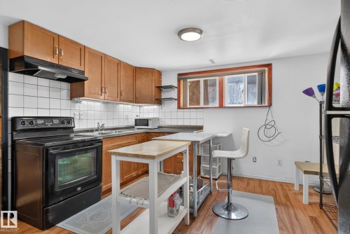Kitchen featuring wood-finish flooring, wood cabinetry, white tile backsplash, and a black electric range - 12229 88 Street Nw, Edmonton, AB - Indoor Photo Showing Kitchen