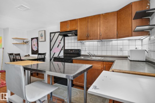 Kitchen featuring wood cabinetry, white tile backsplash, a black range, and an integrated stainless steel sink - 12229 88 Street Nw, Edmonton, AB - Indoor