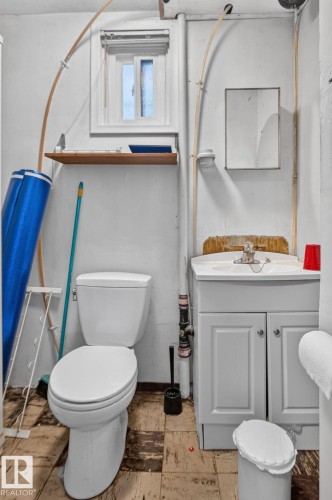Compact bathroom featuring a white toilet, single vanity with cabinet storage, small window, and wall-mounted shelving - 12229 88 Street Nw, Edmonton, AB - Indoor Photo Showing Bathroom