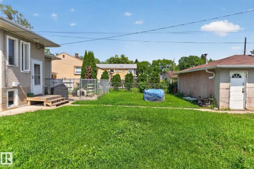 Expansive grassy yard area with a stucco-finish house exterior and a detached garage featuring an arched window door - 12229 88 Street Nw, Edmonton, AB - Outdoor