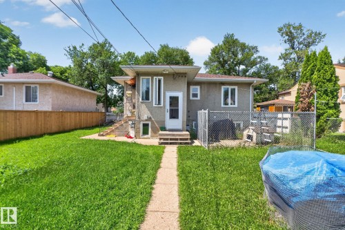 Rear exterior featuring stucco siding, multiple windows, and a partially fenced yard - 12229 88 Street Nw, Edmonton, AB - Outdoor