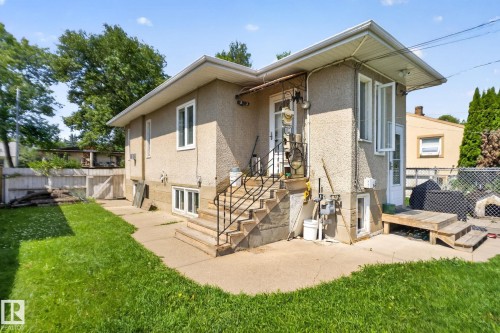 Stucco exterior home featuring a concrete patio, exterior stairs with metal railings, and a side-yard access - 12229 88 Street Nw, Edmonton, AB - Outdoor