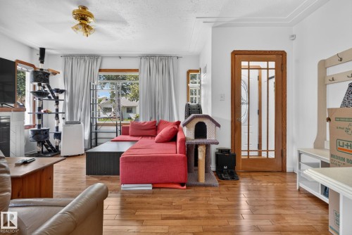 Hardwood flooring extends throughout this interior space, featuring a wood-framed glass-paneled door - 12229 88 Street Nw, Edmonton, AB - Indoor Photo Showing Living Room With Fireplace