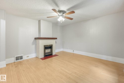 Living area featuring light wood-finish flooring, a white brick fireplace with a dark wood mantel, and a ceiling fan with integrated lighting - 9824 91 Avenue Nw, Edmonton, AB - Indoor With Fireplace