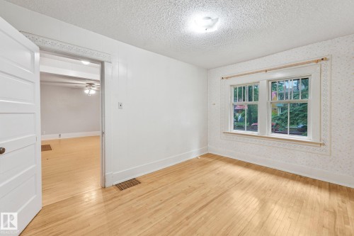Bright room featuring wood-finish flooring, white trim, and a double window with exterior tree views - 9824 91 Avenue Nw, Edmonton, AB - Indoor Photo Showing Other Room