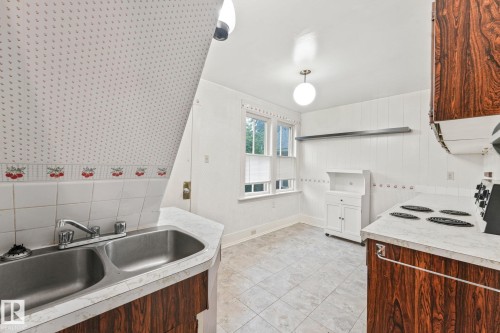 Kitchen area featuring a double basin stainless steel sink with a chrome faucet, wood-finish cabinetry, white countertop surfaces, and tile flooring - 9824 91 Avenue Nw, Edmonton, AB - Indoor Photo Showing Kitchen With Double Sink