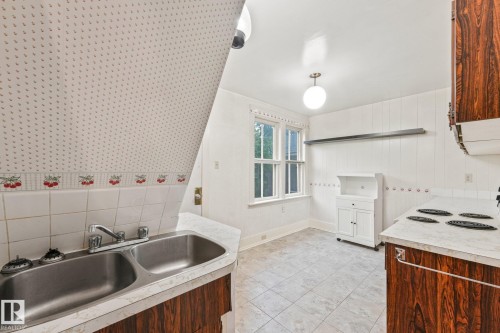 Kitchen featuring a double basin stainless steel sink, wood-finish cabinetry, and a countertop range - 9824 91 Avenue Nw, Edmonton, AB - Indoor Photo Showing Kitchen With Double Sink