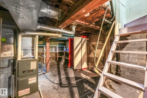 Utility room featuring exposed wooden ceiling joists, a furnace with associated ductwork, a wooden staircase, concrete flooring, and built-in wooden shelving - 9824 91 Avenue Nw, Edmonton, AB - Indoor Photo Showing Basement