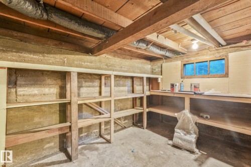 Open basement space featuring exposed wood beam ceiling, concrete walls, built-in wooden shelving, and a small window - 9824 91 Avenue Nw, Edmonton, AB - Indoor