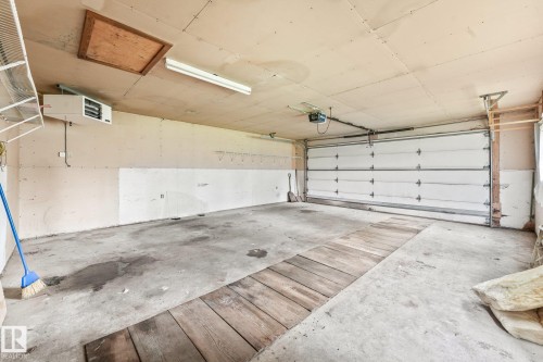 Spacious garage featuring a concrete floor, overhead fluorescent lighting, an automatic garage door opener, an attic access panel, and wall-mounted shelving - 9824 91 Avenue Nw, Edmonton, AB - Indoor Photo Showing Garage