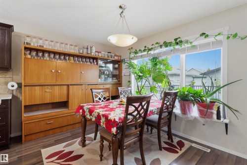 Dining area featuring a large window, wood-finish flooring, a contemporary ceiling light fixture, a built-in wood-tone storage unit, and dark cabinetry - 1528 35 Avenue Nw, Edmonton, AB - Indoor Photo Showing Dining Room