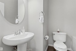 Pedestal sink with chrome faucet, oval mirror, white toilet, and wood-finish flooring - 