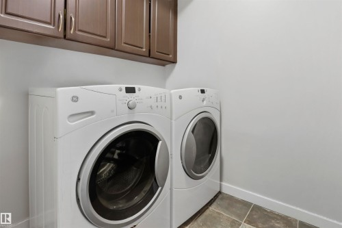 Laundry area featuring neutral wall paint, overhead cabinetry with panel doors and silver-tone hardware, and square floor tiles - 1528 35 Avenue Nw, Edmonton, AB - Indoor Photo Showing Laundry Room