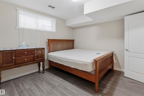 Bright room featuring wood-finish flooring, a window with sheer curtains, a white panel door, and neutral wall paint - 1528 35 Avenue Nw, Edmonton, AB - Indoor Photo Showing Bedroom