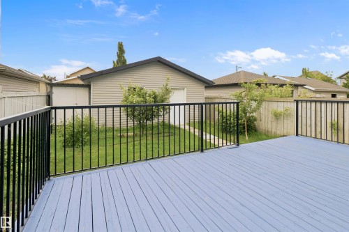 Expansive outdoor deck with light blue wood-finish flooring and black metal railings, overlooking a fenced backyard with a detached garage and mature trees - 1528 35 Avenue Nw, Edmonton, AB - Outdoor With Deck Patio Veranda With Exterior