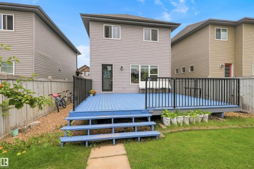 Rear exterior featuring a blue-painted deck with black metal railings, a manicured lawn, and a light gray vinyl siding facade - 1528 35 Avenue Nw, Edmonton, AB - Outdoor With Deck Patio Veranda With Exterior