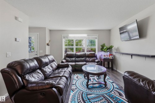 Spacious living area featuring wood-finish flooring, ample natural light from large windows, light gray wall tones, and a wall-mounted shelving unit - 1528 35 Avenue Nw, Edmonton, AB - Indoor Photo Showing Living Room
