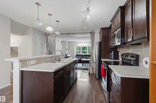 Kitchen featuring wood-finish flooring, dark wood cabinetry, light countertops, and a tile backsplash - 1528 35 Avenue Nw, Edmonton, AB - Indoor Photo Showing Kitchen With Double Sink
