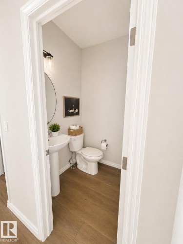 Powder room featuring a pedestal sink, a wall-mounted light fixture, and wood-finish flooring - 1327 20 Nw, Edmonton, AB - Indoor Photo Showing Bathroom
