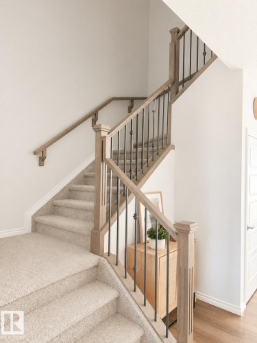 Two-story staircase featuring light wood-finish railings, dark metal balusters, and neutral-toned carpeting - 1327 20 Nw, Edmonton, AB - Indoor Photo Showing Other Room