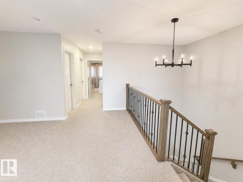Carpeted upper landing featuring a black chandelier, light gray walls, white baseboards, and a wood-finish staircase railing with black iron balusters - 1327 20 Nw, Edmonton, AB - Indoor Photo Showing Other Room