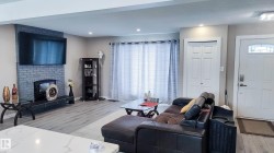 Living area featuring a gray brick fireplace with mantel, wood-finish flooring, recessed lighting, and a white entry door with an arched glass insert - 