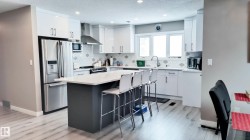 Modern kitchen featuring a central island with a light-colored countertop, stainless steel appliances, white cabinetry, a decorative backsplash, and wood-finish flooring - 