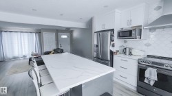 Kitchen featuring a large central island with a light-toned, veined countertop, white cabinetry with silver-toned hardware, and a patterned backsplash - 