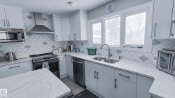 Modern kitchen featuring white cabinetry, a hexagonal tiled backsplash with contrasting accents, and light-toned, veined countertops - 