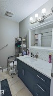 Modern vanity featuring a white countertop with integrated sink, dark cabinetry with bar pull hardware, and geometric tile backsplash - 