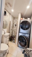 Compact bathroom featuring a glass-enclosed shower, pedestal sink, and stackable laundry appliances - 