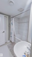 Bathroom featuring a white bathtub, white subway tile surround with subtle veining, and a round basin sink - 