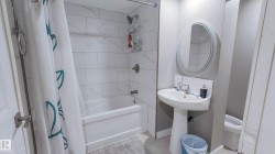 Bathroom featuring a pedestal sink, oval mirror, and a full-size bathtub with subway tile surround - 