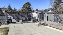 Spacious paved patio featuring a pergola, a grey shed with skylights, and a rock garden border - 