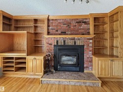 Built-in oak cabinetry and shelving flanking a brick-faced fireplace with a black metal insert - 