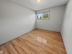 Room featuring wood-finish flooring, light grey painted walls, and a window with wood trim - 