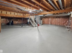Expansive unfinished basement featuring a concrete floor, exposed wooden joists, and a utility staircase - 