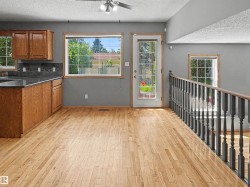 Hardwood flooring throughout a kitchen area featuring wood cabinetry, dark countertops, and a tile backsplash - 