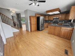 Kitchen featuring wood cabinetry, stainless steel appliances, dark countertops, a tile backsplash, and light wood-finish flooring - 