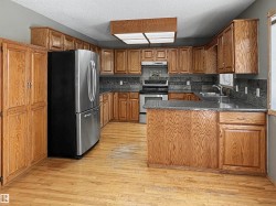 Kitchen featuring wood-finish cabinetry, stainless steel appliances, dark stone countertops, and a gray tile backsplash - 