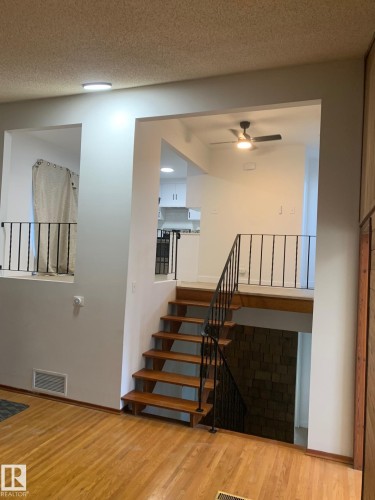 Hardwood flooring throughout the main level featuring a wooden staircase with black wrought iron railings - 16321 - 109A Ave Nw, Edmonton, AB - Indoor Photo Showing Other Room With Fireplace